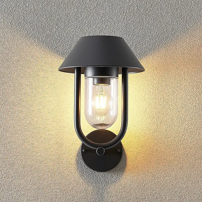 Lucande Außenwandleuchte Olinum - schwarz, schwarz, IP44 - Schwarze Wandleuchte aus Metall mit Klarglas und freiliegender Glühbirne, beleuchtet eine strukturierte Wand.