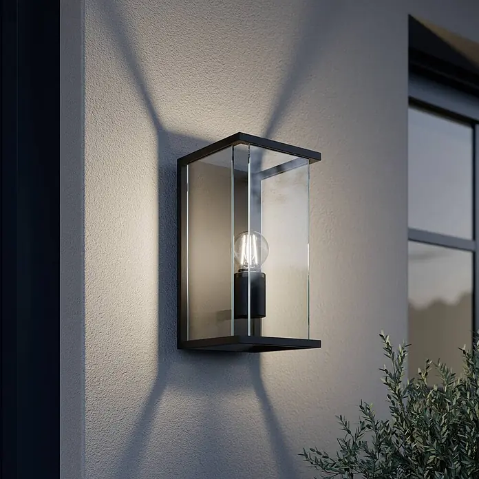 Lucande Außenwandleuchte Annalea - schwarz, klar / transparent, IP54 - Schwarze Außenwandleuchte mit Klarglas und Vintage-Glühbirne, an einer strukturierten Wand montiert, die Lichtmuster wirft.