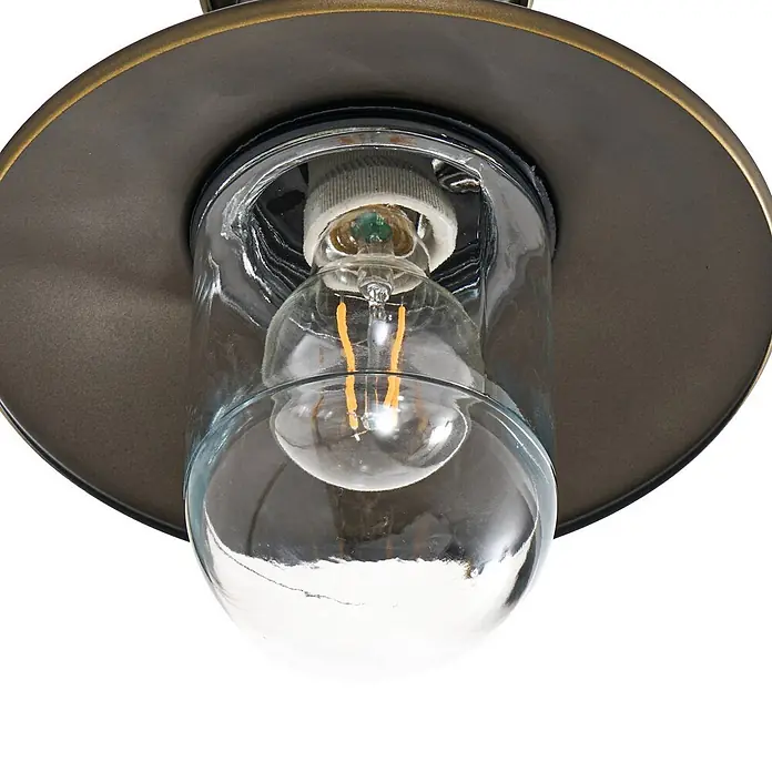 Lindby Außenwandleuchte Eloretta - messing / gold, messing / gold, IP44 - Nahaufnahme einer Deckenleuchte mit dunklem Bronzemetallsockel, klarem Glasschirm und sichtbarer LED-Filamentlampe.