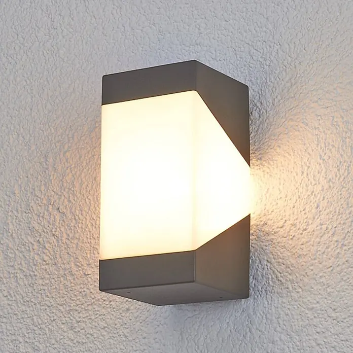 Lucande Außenwandleuchte Kiran - schwarz, IP44 - Graue rechteckige Außenwandleuchte mit leuchtendem weißem Diffusor, die eine strukturierte Wand warm beleuchtet.