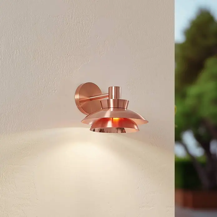 Lucande Außenwandleuchte Thais - kupfer, IP44 - Kupferfarbene Wandleuchte mit Lamellen, an einer strukturierten Wand montiert, warmes Licht ausstrahlend.