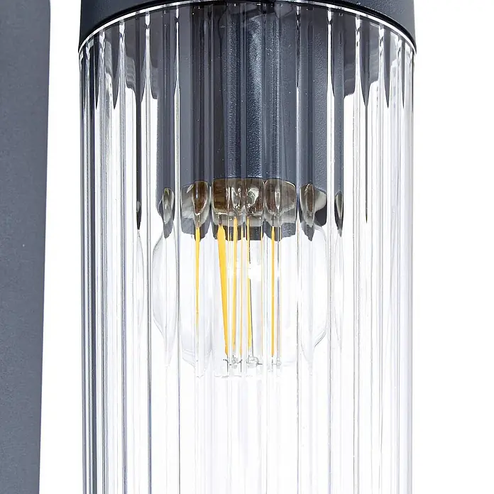 Lindby Außenwandleuchte Kaliro - 13,8 x 8 x 23,4 cm, schwarz, klar / transparent, IP54 - Nahaufnahme einer dunkelgrauen Außenleuchte mit transparentem, geriffeltem Glaszylinder und LED-Filamentlampe.