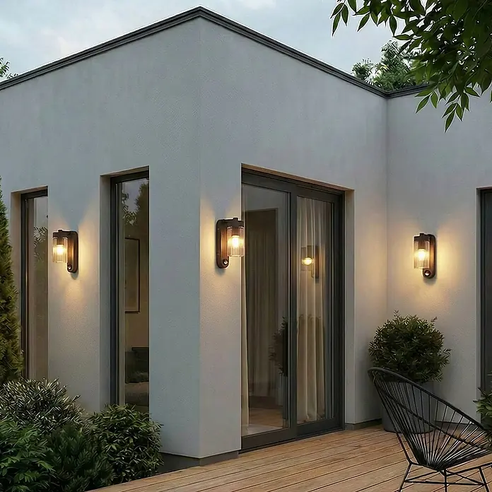 Lindby Außenwandleuchte Kaliro - 13,8 x 8 x 23,4 cm, schwarz, klar / transparent, IP54 - Drei moderne Außenwandleuchten mit dunklen Metallsockeln und gerippten Glasschirmen beleuchten eine Hausfassade und Holzterrasse.