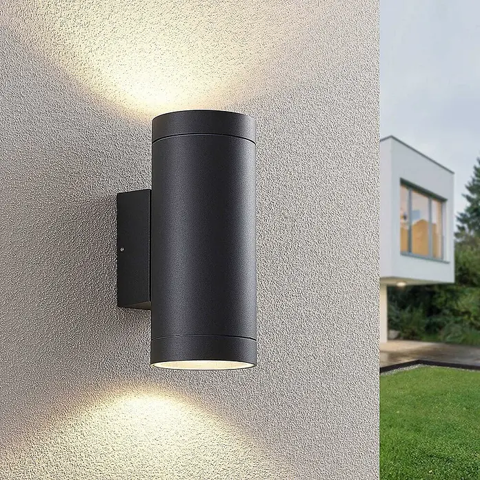 Lucande Außenwandleuchte Thomke - alu / grau / zink, alu / grau / zink, IP65 - Schwarze zylindrische Außenwandleuchte an strukturierter Wand, die warmes Licht nach oben und unten abgibt.