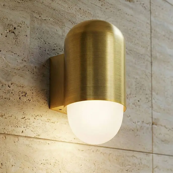 Lindby Außenwandleuchte Pilva - bronze / altmessing, weiß / opal, IP44 - Wandleuchte aus gebürstetem Messing mit mattem Glasdiffusor, an einer strukturierten Wand montiert.