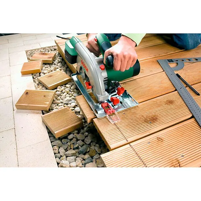 Bosch Handkreissäge PKS 66 AF - 1.600 W, 5.000 U/min - Akkutischkreissäge im Einsatz zum Schneiden von Holzbrettern, mit Steinen und Ziegeln im Hintergrund, ideal für Heimwerkerprojekte.