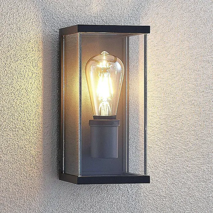 Lindby Außenwandleuchte Susanne - 13 x 12 x 25 cm, schwarz, IP44 - Rechteckige schwarze Außenwandleuchte mit Klarglaspaneelen und einer glühenden Edison-Glühbirne, an einer strukturierten Wand montiert.