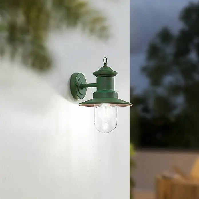 Lindby Wandlampe außen Laterne rustikal grün, Wandleuchte aussen IP44 -  - Grüne Außenwandleuchte mit klarem Glasschirm und sichtbarer Glühbirne, an einer weißen Wand in der Dämmerung montiert.