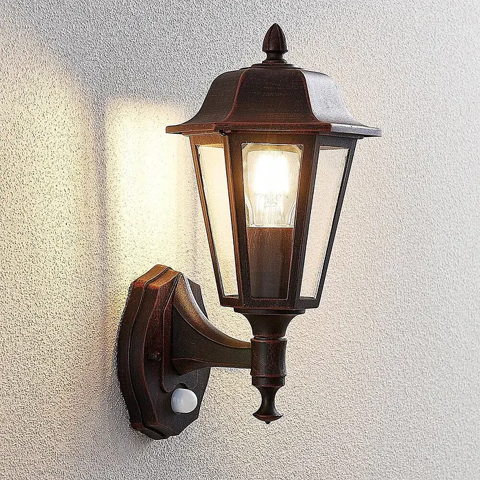 Lindby Außenwandleuchte Noor - schwarz, schwarz, IP44 - Dunkelbronzene Außenwandleuchte mit Glasscheiben und Bewegungssensor, beleuchtet an einer strukturierten Wand.
