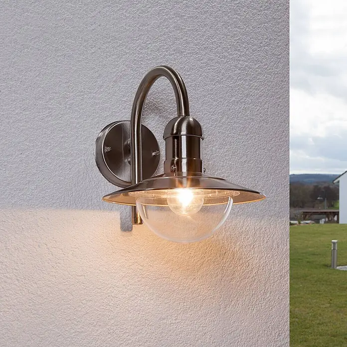 Lindby Außenwandleuchte Damion - alu / grau / zink, IP44 - Gebürstete Edelstahl-Außenwandleuchte mit klarer Glaskuppel, die warmes Licht an eine strukturierte Wand abgibt.