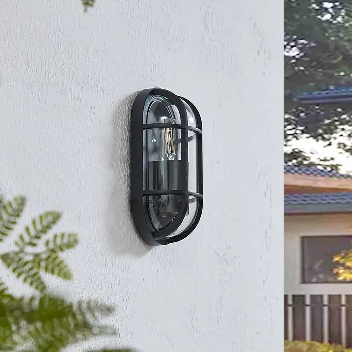 Lucande Außenwandleuchte Serine - schwarz, klar / transparent, IP65 - Schwarze ovale Außenwandleuchte mit Klarglas und Filamentlampe, an einer weißen Strukturwand montiert.