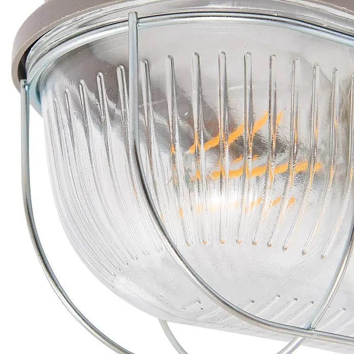 Prios Außenwandleuchte Kirgo - 11,3 x 16 x 12,5 cm, alu / grau / zink, IP44 - Nahaufnahme einer Industrielampe mit geriffeltem Glasschirm, Metallgitter und grauem Sockel. Eine LED-Glühbirne ist sichtbar.