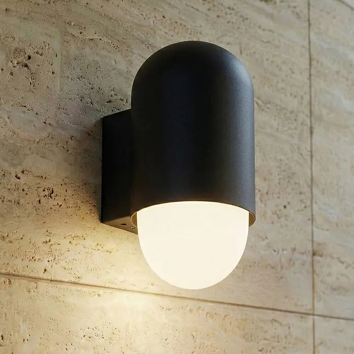 Lindby Wandleuchte aussen in schwarz, weiß, Aussenlampe Wand -  - Schwarze Außenwandleuchte mit leuchtendem weißem Diffusor, an einer strukturierten Steinwand montiert.