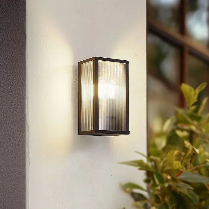 Lindby Außenwandleuchte Peldar - 13,5 x 14 x 26 cm, schwarz, IP44 - Rechteckige Außenwandleuchte mit dunklem Rahmen und geriffeltem Glas, die eine Wand warm beleuchtet.