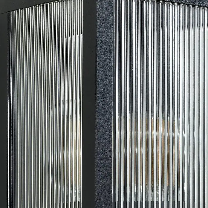 Lindby Außenwandleuchte Peldar - 13,5 x 14 x 26 cm, schwarz, IP44 - Dunkel gerahmte Leuchte mit klaren, geriffelten Glaspaneelen, die eine interne Lichtquelle zeigt.