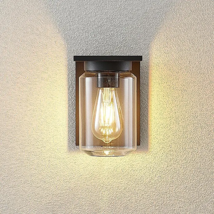 Lucande Außenwandleuchte Semka - schwarz, klar / transparent, IP54 - Moderne Wandleuchte mit klarem Glasschirm und Edison-Glühbirne, an einer strukturierten Wand montiert und warmes Licht spendend.