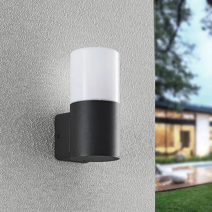 Lindby Außenwandleuchte Tabyn - schwarz, IP44 - Schwarze Außenwandleuchte mit weißem zylindrischem Diffusor, an einer texturierten Wand montiert, im Außenbereich.