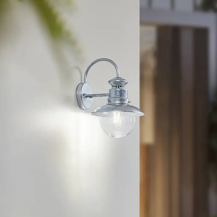 Lindby Außenwandleuchte Celinor - chrom / silber, chrom / silber, IP44 - Wandleuchte aus verzinktem Metall mit klarer Glaskugel, an einer Wand montiert und beleuchtet.