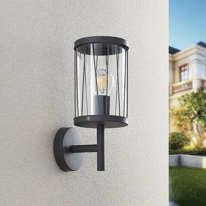 Lindby Außenwandleuchte Yonan - schwarz, schwarz, IP44 - Schwarze Außenwandleuchte mit klarem Zylinderglas und Vintage-LED-Birne an strukturierter Außenwand.