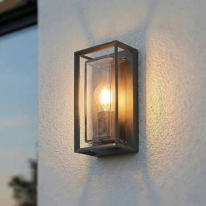 Arcchio Außenwandleuchte Ismera - schwarz, schwarz, IP65 - Moderne dunkelgraue Außenwandleuchte mit Klarglas und beleuchteter Glühbirne an einer strukturierten Wand.
