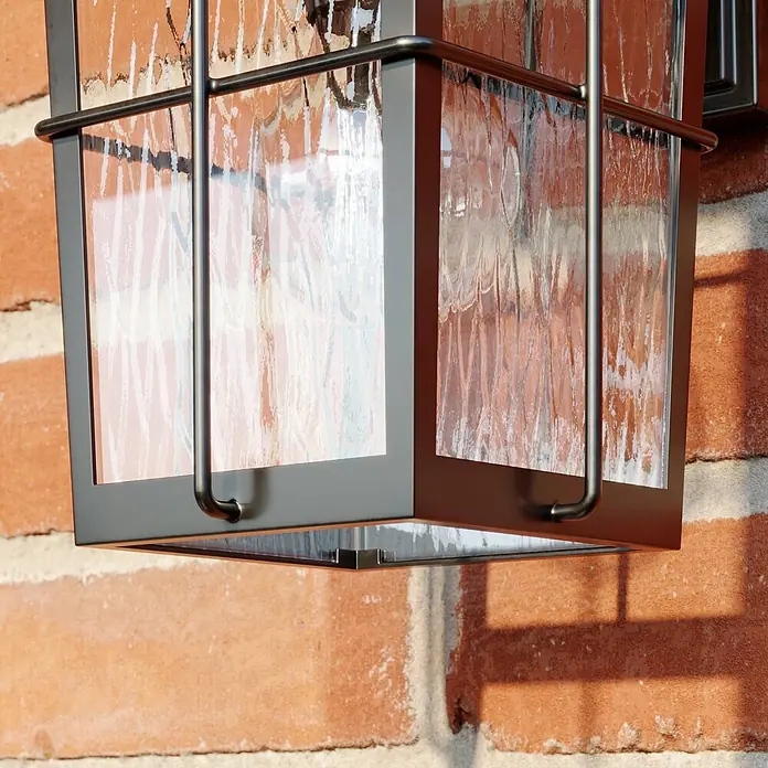 Lindby Außenwandleuchte Charmaine - 18,6 x 15,3 x 28,6 cm, braun / rost, braun / rost, IP23 - Dunkle Metall-Wandleuchte mit strukturierten Glaspaneelen, an einer Ziegelwand montiert.