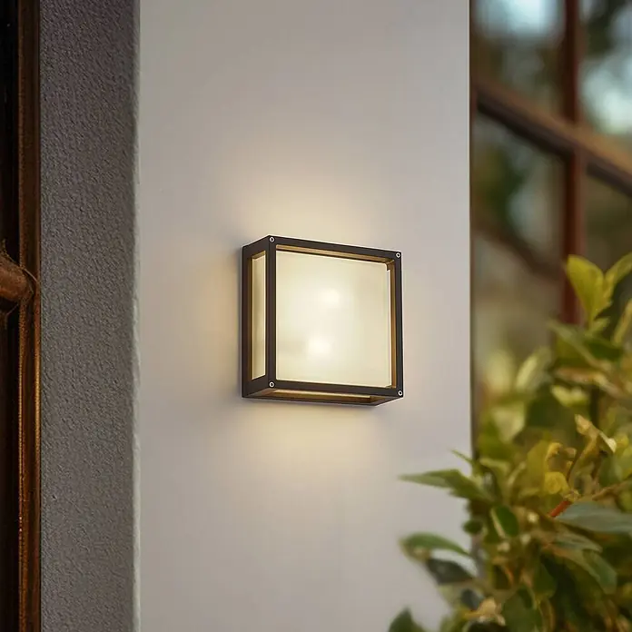 Lucande Außenwandleuchte Aurelien - schwarz, IP54 - Quadratische Außenwandleuchte mit schwarzem Rahmen und diffusem weißen Panel, beleuchtet und an einer Hauswand montiert.