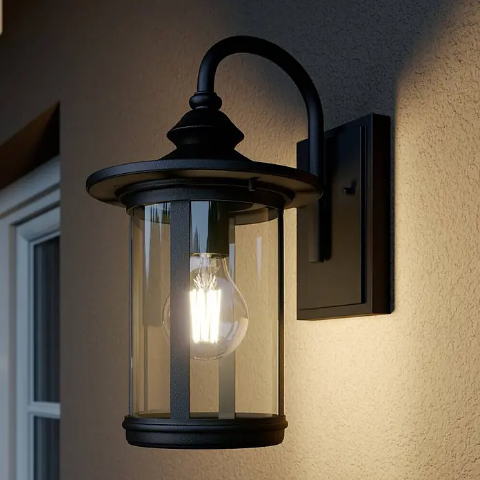 Lindby Außenwandleuchte Zayn - 23,8 x 19 x 33,4 cm, schwarz, IP23 - Schwarze Außenwandleuchte aus Metall mit Klarglas und LED-Glühlampe an einer strukturierten Wand.