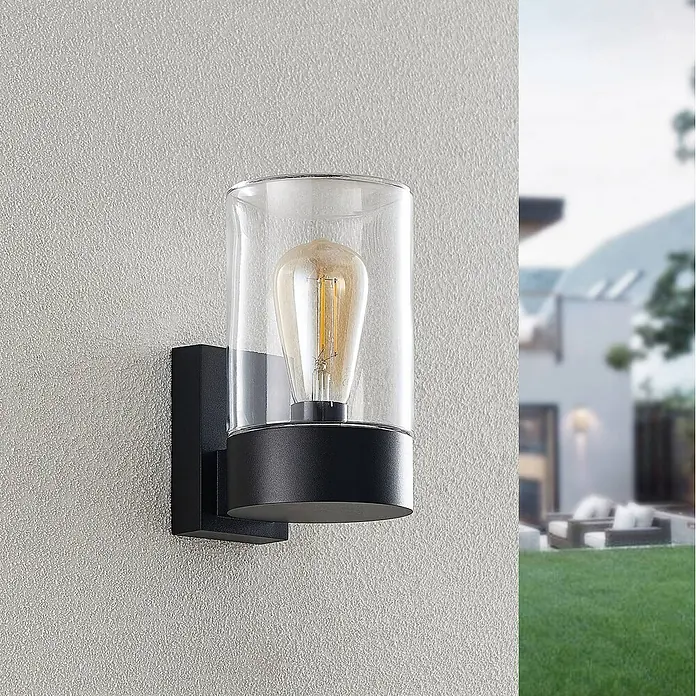 Arcchio Außenwandleuchte Liljana - schwarz, klar / transparent, IP65 - Schwarze Außenwandleuchte mit klarem Glaszylinder und Vintage-LED-Birne. An einer Außenwand montiert.