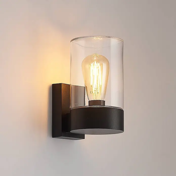 Arcchio Außenwandleuchte Liljana - schwarz, klar / transparent, IP65 - Schwarze Wandleuchte mit klarem Glaszylinder und sichtbarer Edison-Birne, die warmes Licht abstrahlt.