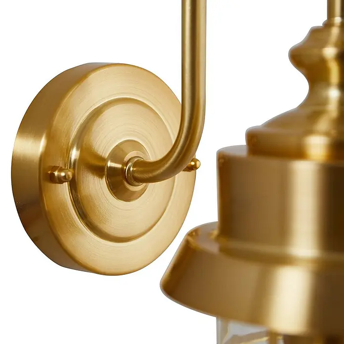 Lindby Außenwandleuchte Adalie - 21,5 x 13,7 x 31 cm, messing / gold, IP44 - Nahaufnahme einer gebürsteten goldfarbenen Wandleuchte mit gebogenem Arm und rundem Sockel.