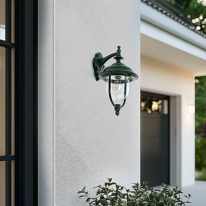 Lindby Außenwandleuchte Clint - grün, IP44 - Dunkelgrüne Außenwandleuchte mit Glaskugel und Edison-Birne, an einer strukturierten weißen Wand neben einem Fenster montiert.
