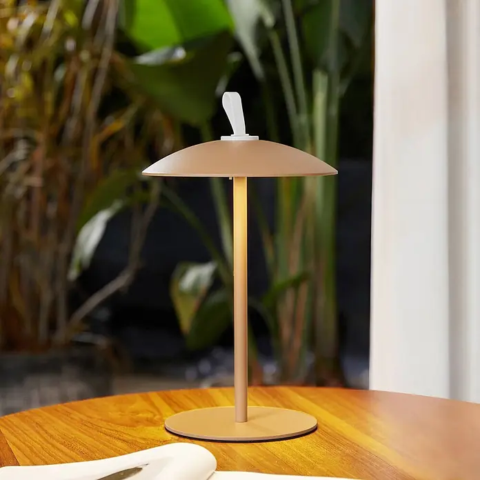 Lindby LED-Tischleuchte Kanani - braun / rost, braun / rost, Warmweiß - Eine beleuchtete beige tragbare Tischlampe mit pilzförmigem Schirm und weißem Griff auf einem Holztisch.