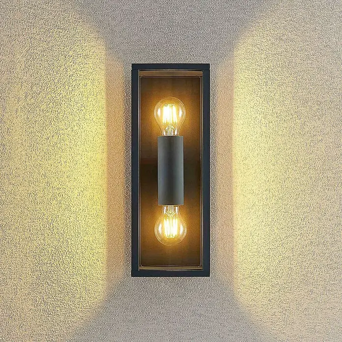 Lindby Außenwandleuchte Peldar - schwarz, IP44 - Dunkle rechteckige Außenwandleuchte mit zwei LED-Filamentlampen, die warmes Licht nach oben und unten auf eine strukturierte Wand wirft.