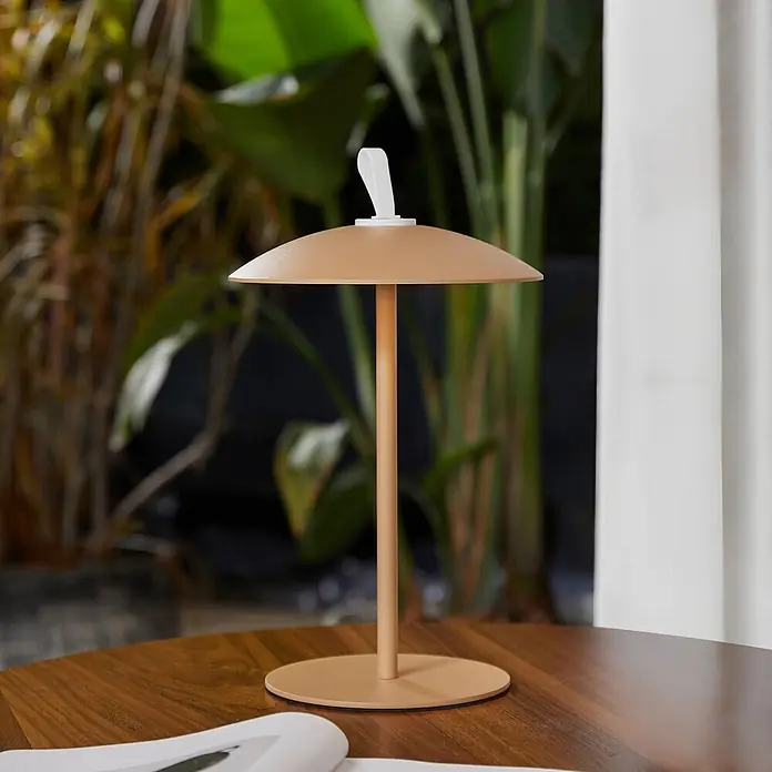 Lindby LED-Tischleuchte Kanani - braun / rost, braun / rost, Warmweiß - Beige Tischlampe mit pilzförmigem Schirm und weißem Griff auf einem Holztisch.