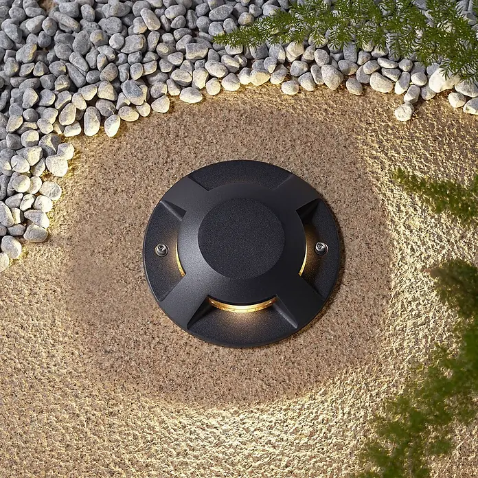 Lucande LED-Gartenstrahler Jeffrey - 3.000 K - Runde, schwarze Einbauleuchte für den Außenbereich, die einen gekörnten Weg und Kieselsteine mit warmem Licht erhellt.