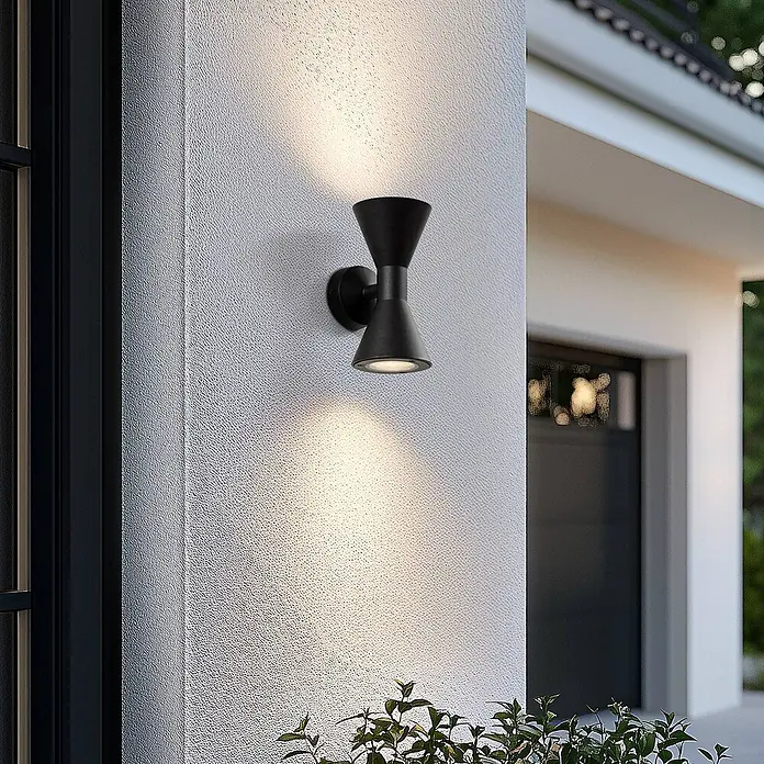 Lucande Außenwandleuchte Xalor - schwarz, IP65 - Schwarze Sanduhr-förmige Außenwandleuchte beleuchtet eine strukturierte weiße Fassade, nach oben und unten leuchtend.