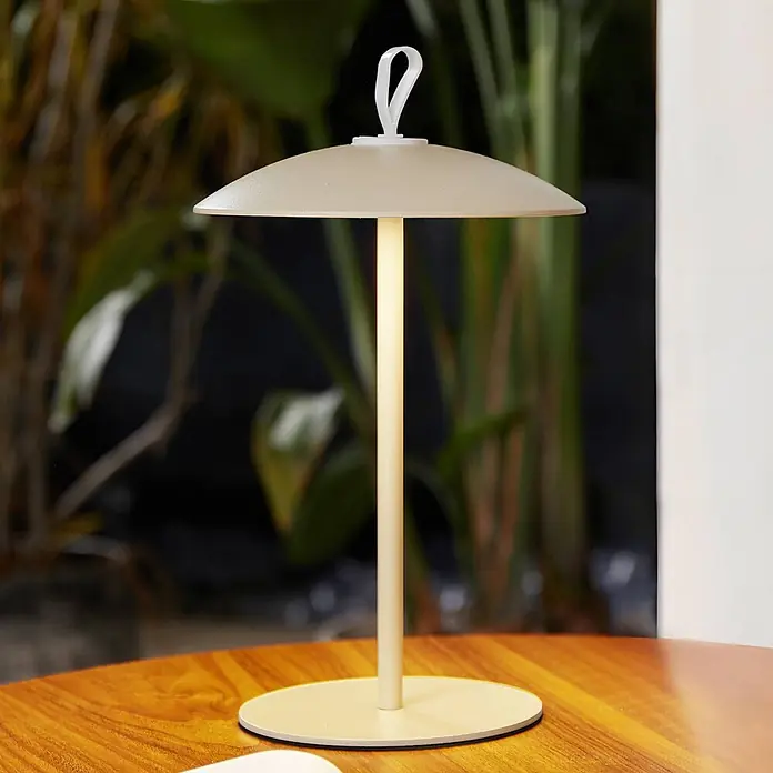 Lindby LED-Tischleuchte Kanani - L x B x H: 18,1 x 18,1 x 30,8 cm, creme / amber, creme / amber, Warmweiß - Beige kabellose Tischlampe mit schirmförmigem Schirm, leuchtendem Stiel und Schlaufe, auf einem Holztisch.