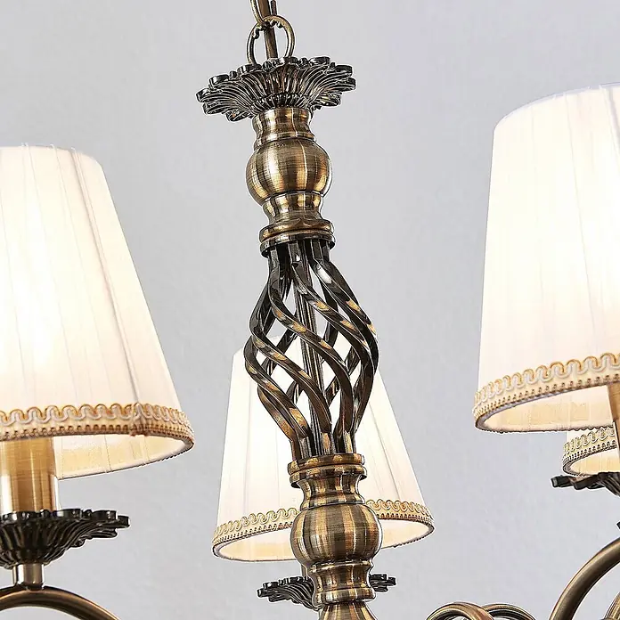 Lindby Kronleuchter Finnick - weiß, altmessing, E14 - Nahaufnahme eines antiken Messingleuchters mit gedrehten Metalldetails und weißen plissierten Stoffschirmen.