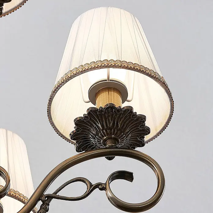 Lindby Kronleuchter Finnick - weiß, altmessing, E14 - Plissierter creme-farbener Lampenschirm mit Zierborte, Messing-Fassung und verzierter Bronze-Kronleuchterarm mit Ranken.