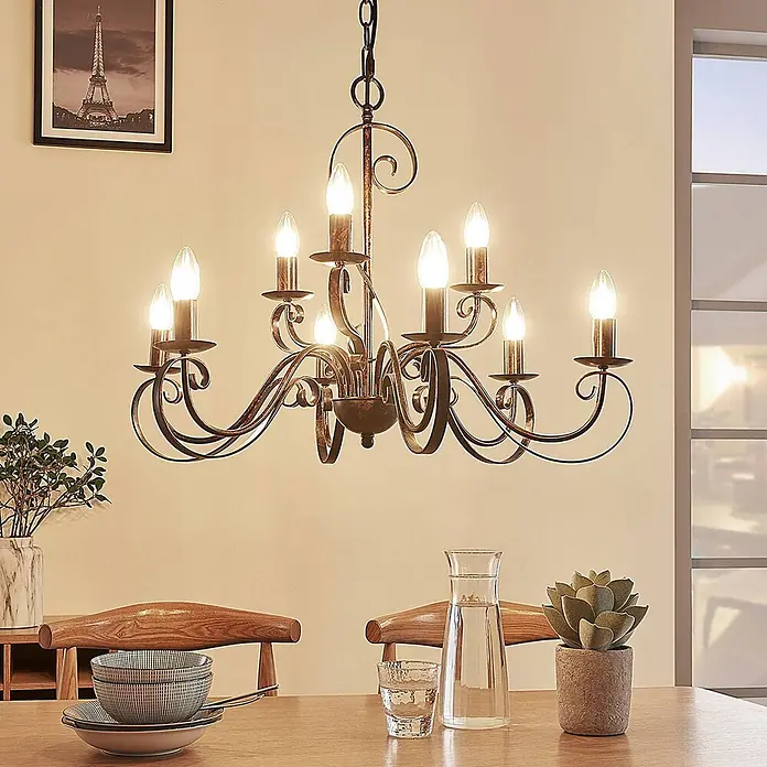 Lindby Kronleuchter Caleb - braun / rost, rostbraun, E14 - Ein Kronleuchter aus antikem Bronze-Schmiedeeisen mit Kerzenlampen über einem Esstisch.
