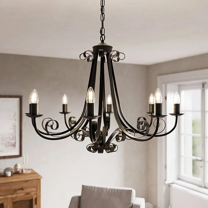Lindby Kronleuchter Scaleria - antikbraun, E14 - Dunkler Metall-Kronleuchter mit Schnörkeln und sechs Kerzenlampen, in einem Wohnzimmer hängend.