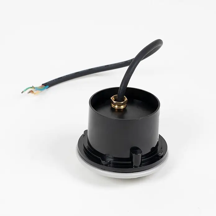 Lindby LED-Gartenstrahler Nandita - 3.000 K - Schwarz zylindrisches Elektroteil mit Messing-Kabelverschraubung und angeschlossenem schwarzem Kabel mit freiliegenden farbigen Adern.
