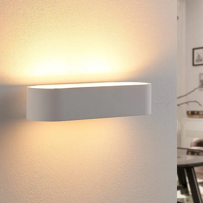Lindby Wandleuchte Fioni - L x B x H: 10,5 x 30 x 6,5 cm, weiß / opal, G9 - Weiße ovale Wandleuchte, die warmes Licht nach oben und unten auf eine strukturierte Wand wirft.