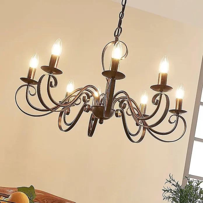 Lucande Kronleuchter Caleb - braun / rost, rostbraun, E14 - Antiker bronzefarbener Kronleuchter mit acht kerzenförmigen Lichtern und geschwungenen Metallarmen, von der Decke hängend.