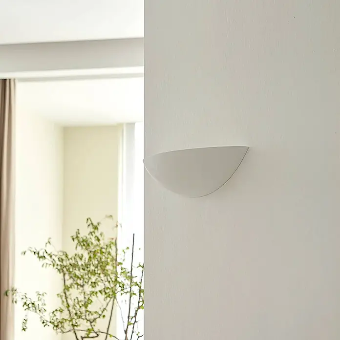 Lindby Wandleuchte Guilia - weiß / opal, weiß / opal, E27 - Weiße, halbkreisförmige Wandleuchte an einer hellen Wand in einem hellen Raum mit Pflanze.