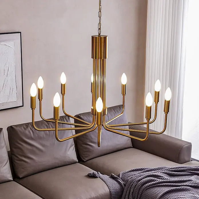 Lindby Kronleuchter Elanova - messing, E14 - Ein goldener Kronleuchter mit zehn weißen Kerzenbirnen hängt über einem grauen Ecksofa im Wohnzimmer.