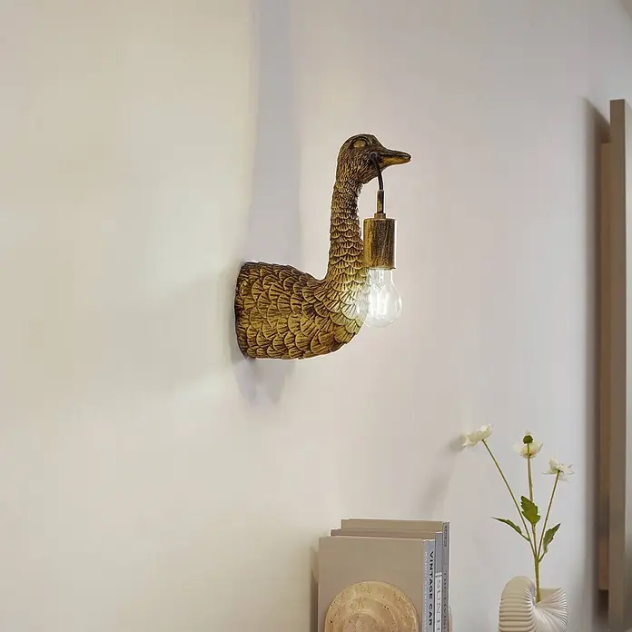 Lindby Wandleuchte Nirvathia - L x B x H: 24,5 x 9 x 30,5 cm, bronze / altmessing, E27 - Antikgoldene Wandleuchte in Entenform, die eine klare Glühbirne im Schnabel hält.