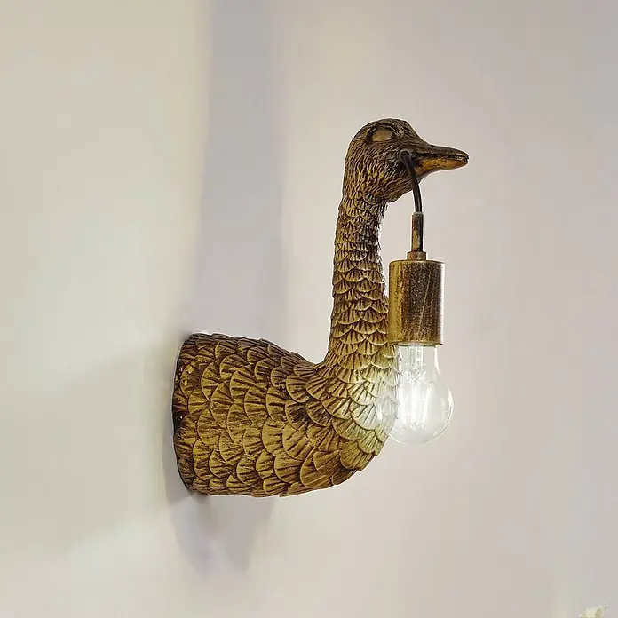 Lindby Wandleuchte Nirvathia - L x B x H: 24,5 x 9 x 30,5 cm, bronze / altmessing, E27 - Goldene Enten-Wandleuchte, die eine Glühbirne im Schnabel hält.