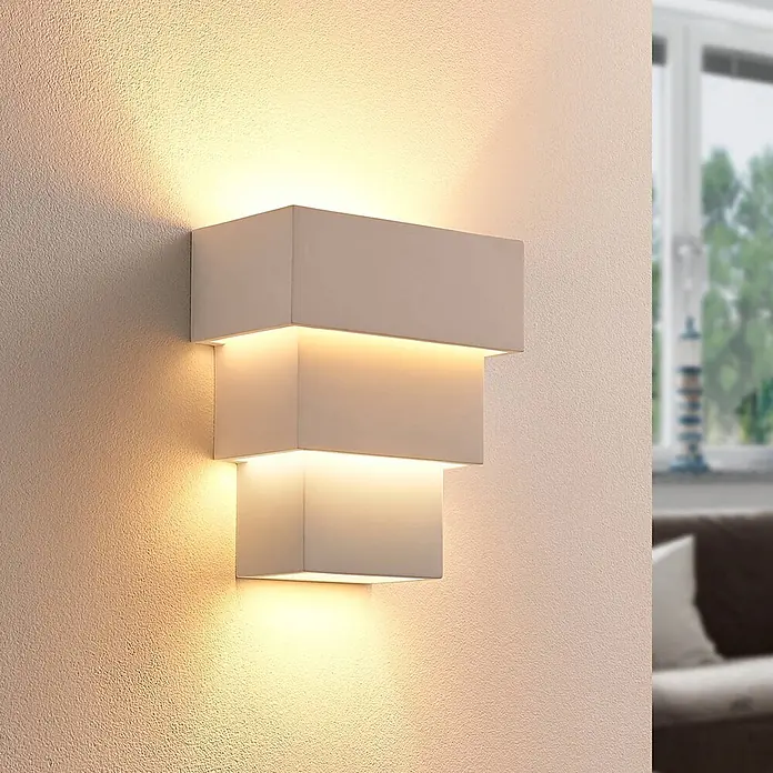 Lindby Wandleuchte Antonella - L x B x H: 10,5 x 18 x 21 cm, weiß / opal, G9 - Moderne weiße, rechteckige Wandleuchte mit gestuften Design, die warmes Auf- und Abwärtslicht auf eine strukturierte Wand in einem Raum wirft.