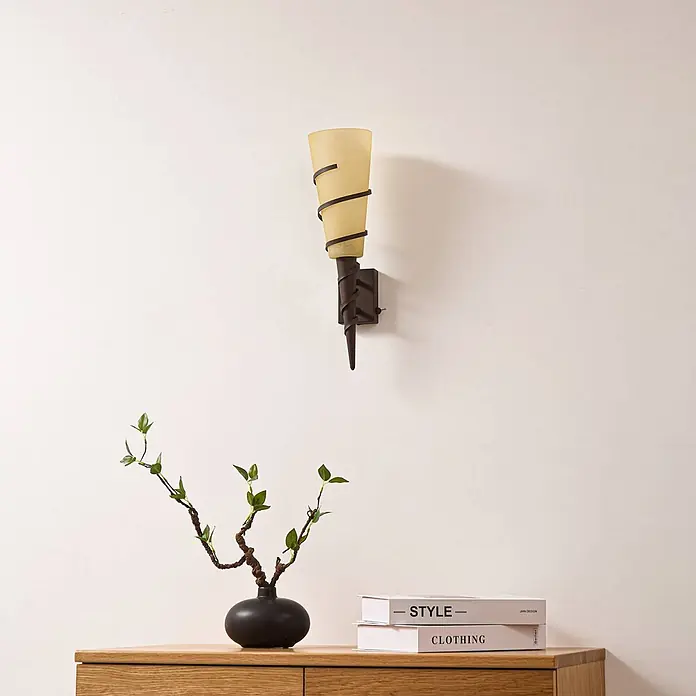 Lindby Wandleuchte Anouk - L x B x H: 16 x 12 x 44 cm, braun / rost, E14 - Wandleuchte mit hellem Glasschirm und dunklen Metallspiralen, über einem Holzschrank montiert.